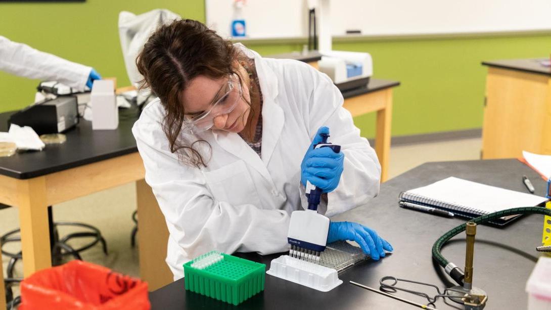 A student in a lab coat and goggles conducts an experiment in a science lab