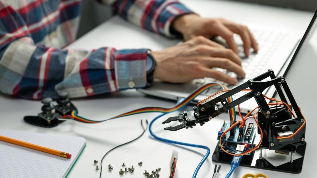 Student hands programming the wiring for a robotic arm