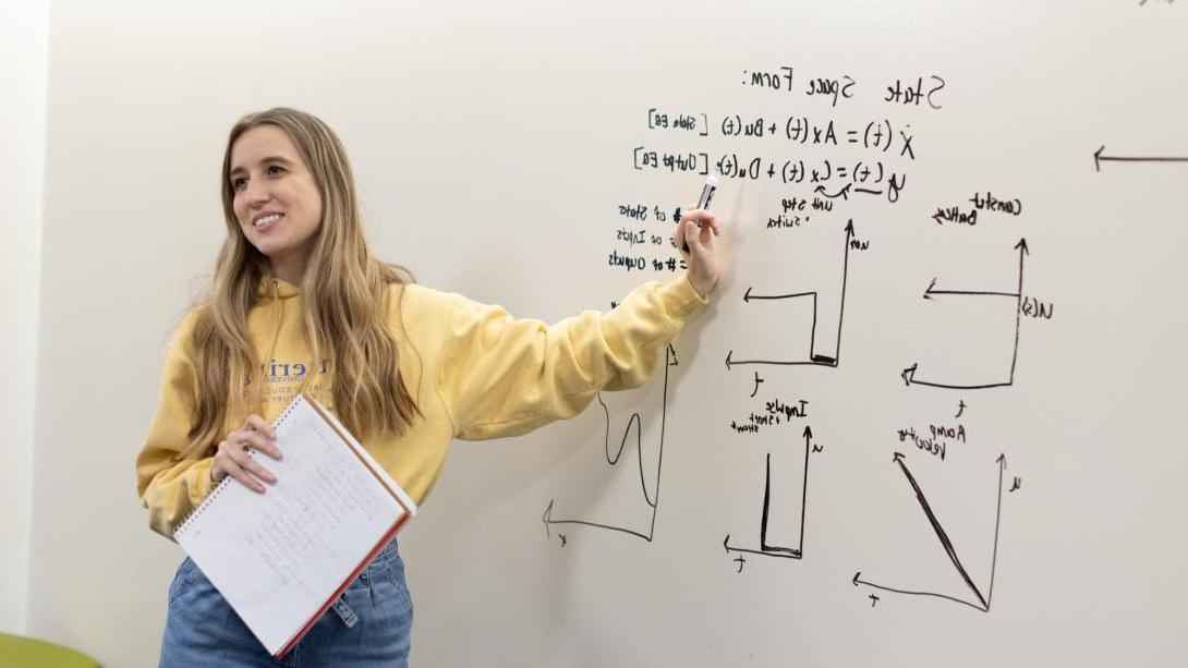 Student standing at a whiteboard with a mathematic problem displayed