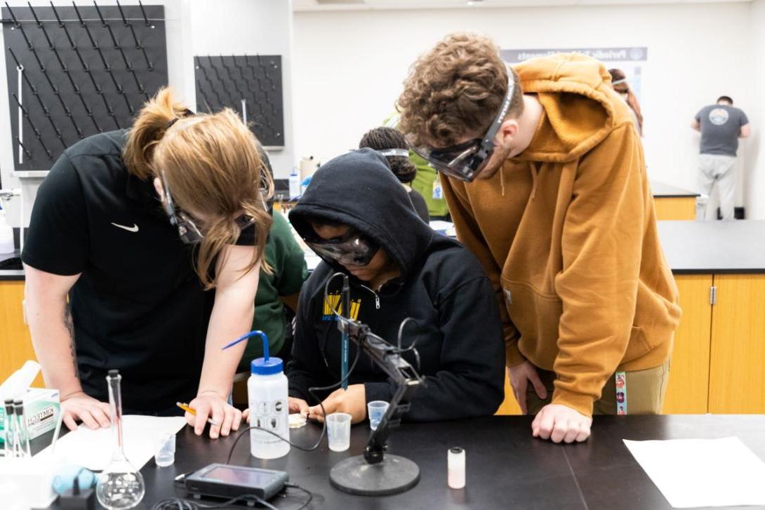 Three people crowd around a microscope